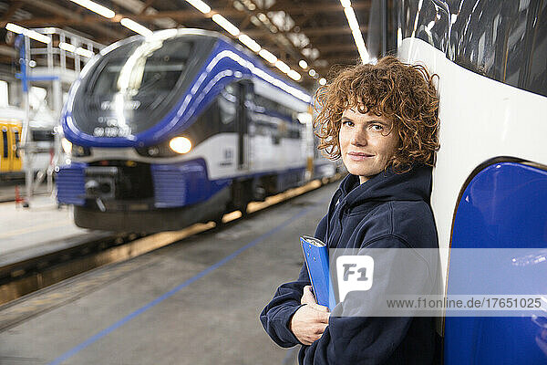 Confident engineer holding file folder leaning on monorail at industry