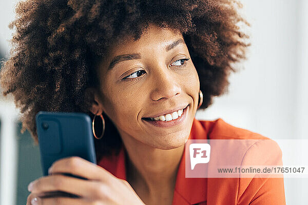 Lächelnde Geschäftsfrau mit Afro-Frisur hält Mobiltelefon in der Hand