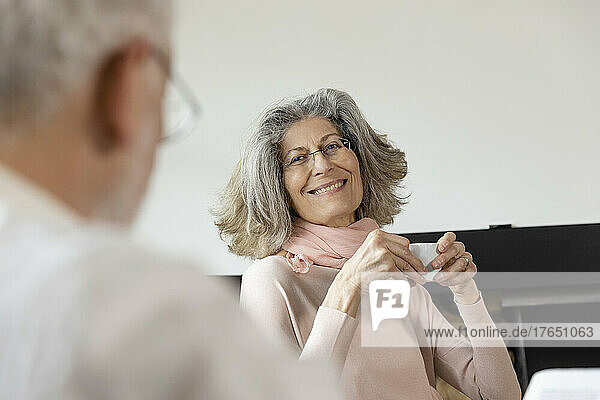 Smiling senior woman holding coffee cup looking at man in living room