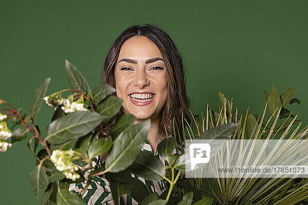 Cheerful woman holding leaves against green background