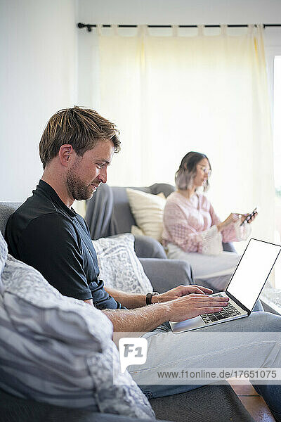 Freelancer working on laptop with woman using mobile phone at home