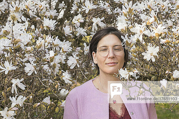 Smiling woman with closed eyes standing amidst blooming magnolia tree