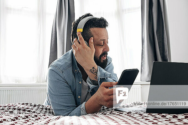 Mann mit kabellosen Kopfhörern nutzt Smartphone zu Hause