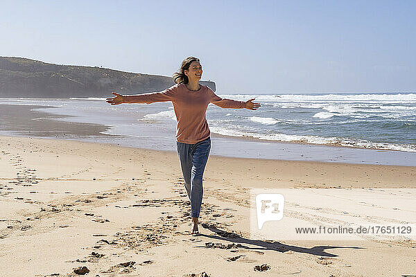 Happy woman with arms outstretched running at beach on sunny day