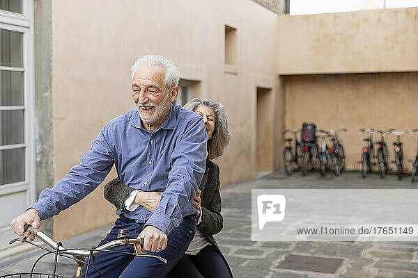 Ältere Frau sitzt mit Mann auf Fahrrad vor Gebäude
