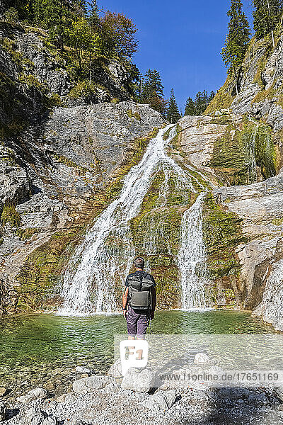 Männlicher Wanderer bewundert den Glasbach-Wasserfall in den Bayerischen Voralpen