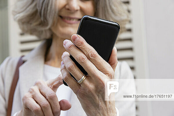 Lächelnde ältere Frau  die mit dem Mobiltelefon im Internet surft