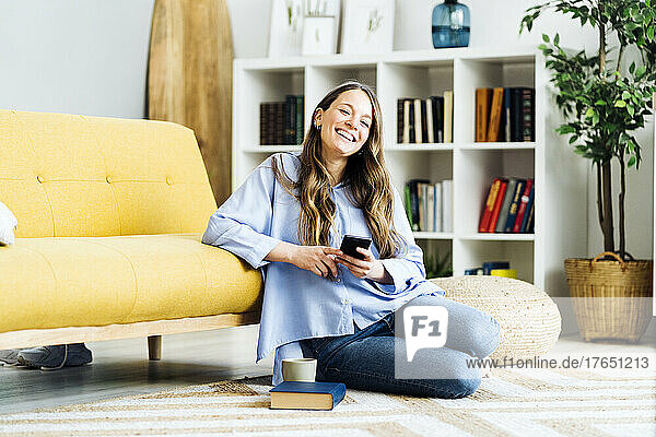 Happy woman with smart phone sitting on carpet at home