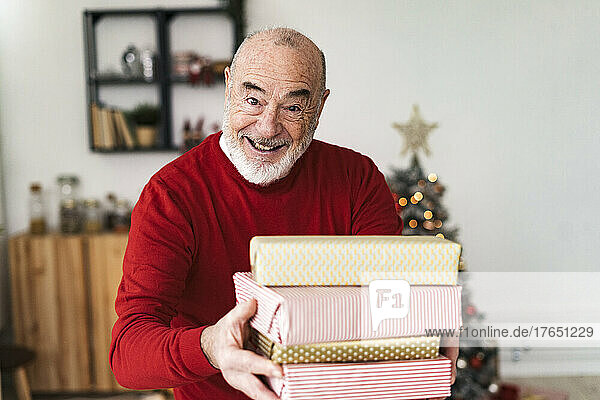 Smiling senior man giving gift boxes at home