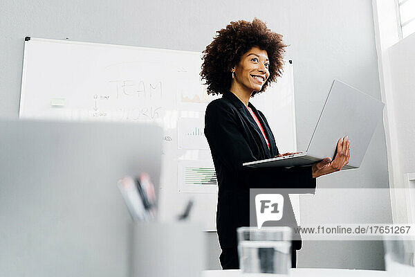 Smiling businesswoman with laptop standing in front of whiteboard
