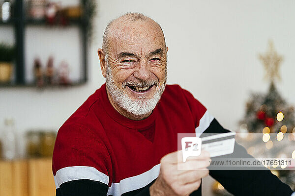 Happy senior man holding credit card at home