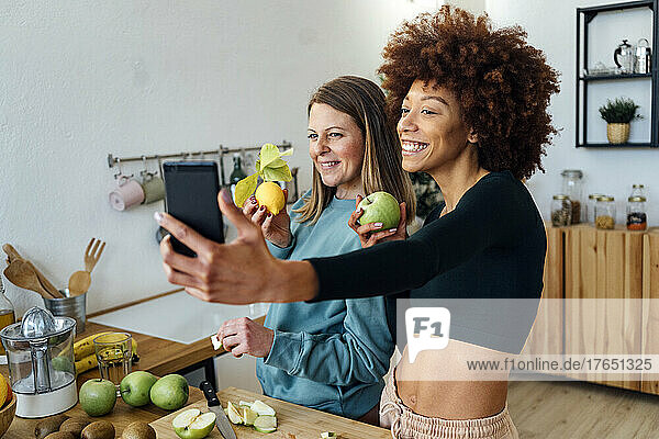 Happy women with fresh fruits taking selfie through smart phone in kitchen at home