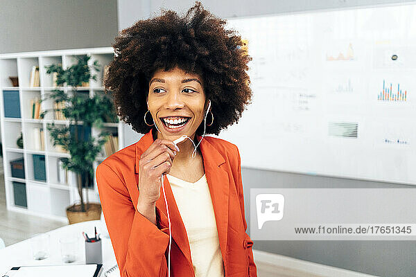 Happy businesswoman talking through in-ear headphones at office