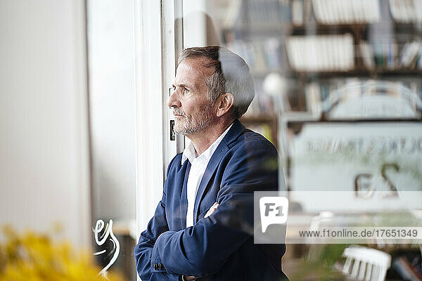 Thoughtful businessman with arms crossed looking through window at cafe