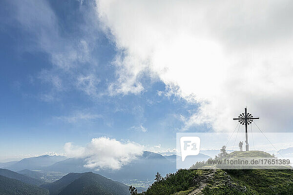 Frau steht am Brunstlkopf-Gipfelkreuz auf dem Berg unter bewölktem Himmel