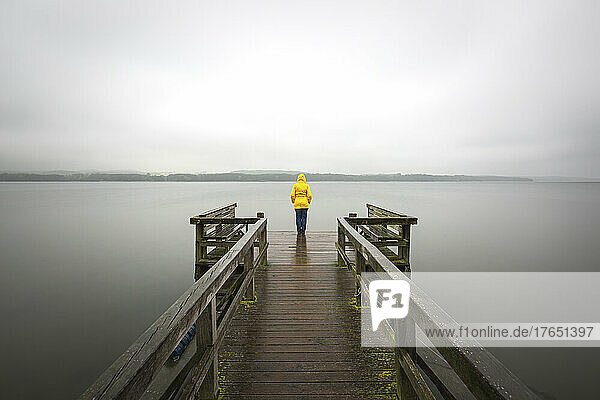 Deutschland  Schleswig-Holstein  Frau in gelber Jacke steht am Rand eines Stegs am Seeufer