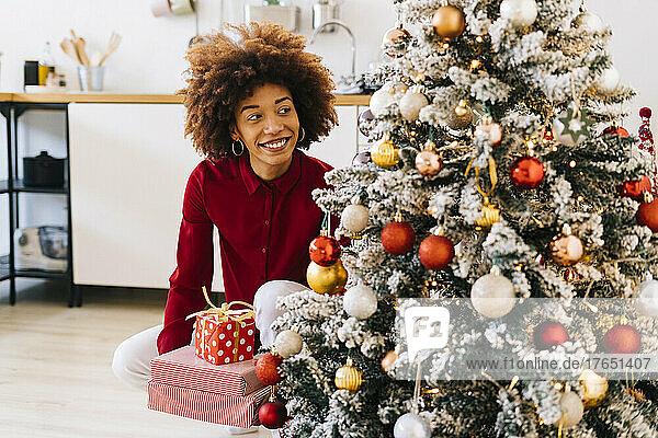 Glückliche Frau mit Geschenken sitzt zu Hause am Weihnachtsbaum