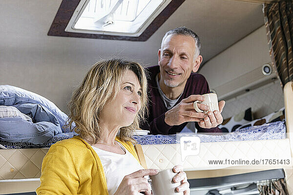 Man looking at thoughtful woman with coffee cup in camper van