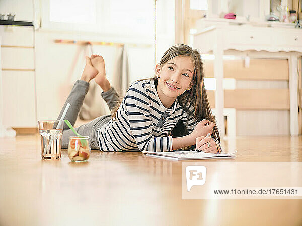 Smiling girl with book lying on floor at home