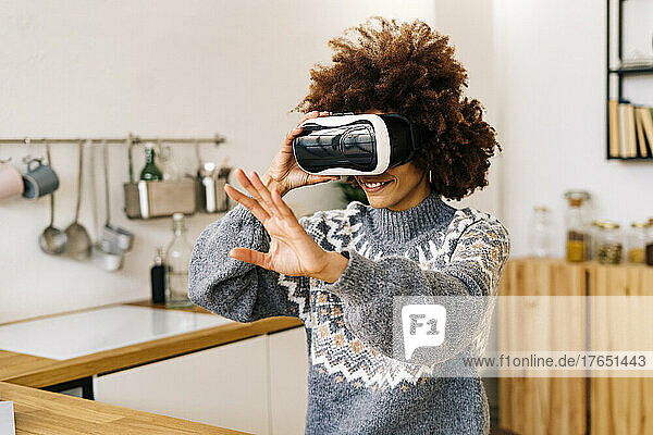 Smiling young woman wearing virtual reality simulator gesturing at home