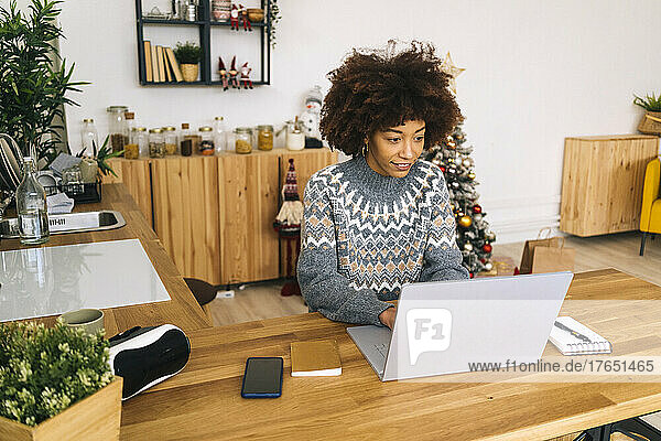 Smiling young woman with Afro hairstyle using laptop sitting at table