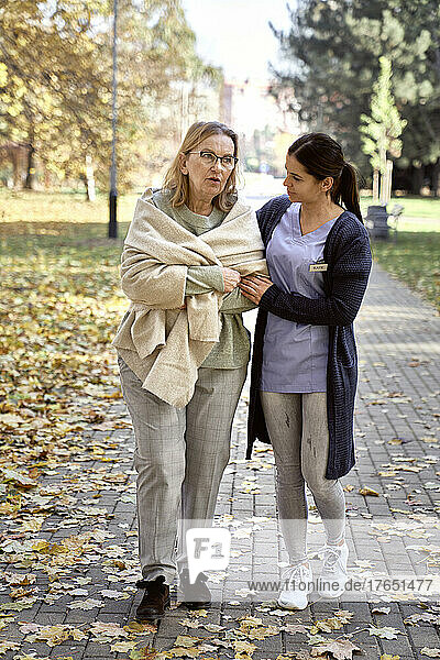 Caretaker looking at senior woman walking on footpath in park