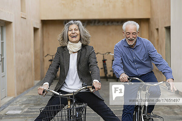 Happy senior couple riding bicycles outside building
