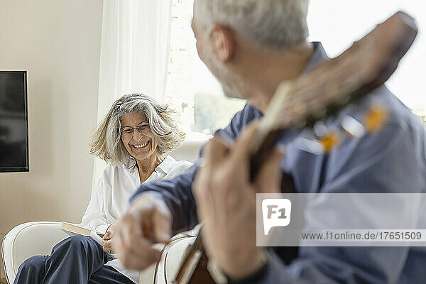 Happy woman looking at man playing guitar at home