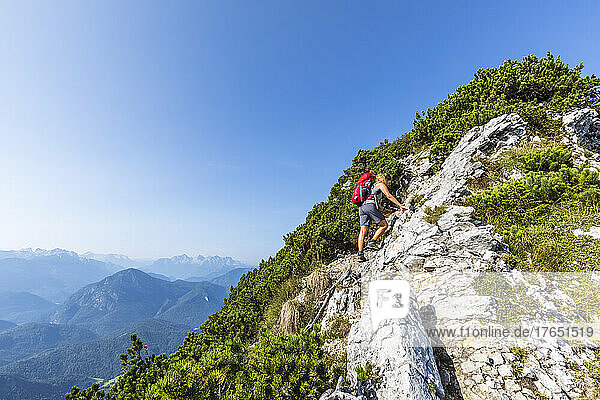Wanderer mit Rucksack klettert an einem sonnigen Tag auf den Berg
