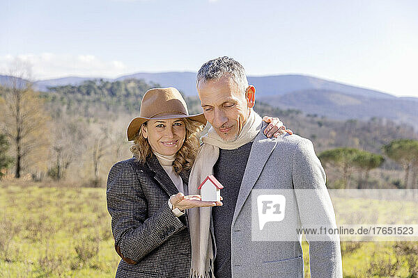 Mature couple holding small house model on sunny day