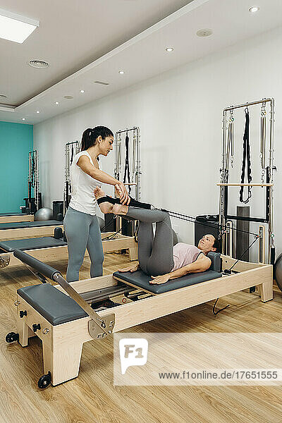 Fitness instructor teaching woman leg exercise at pilates studio