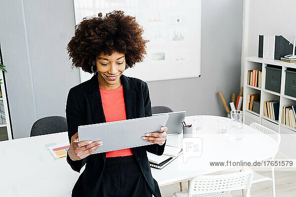 Smiling young businesswoman with Afro hairstyle using tablet PC in office