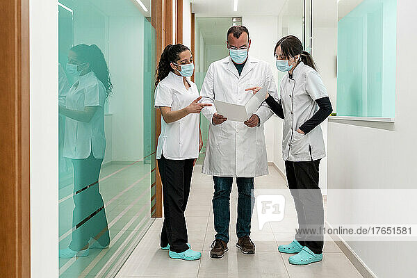 Doctor discussing medical report with nurses in corridor at hospital