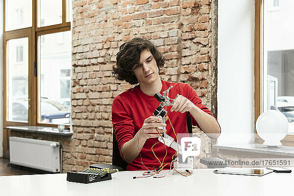 Teenager arbeitet am Roboterarm und sitzt am Tisch