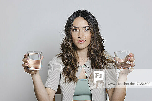 Beautiful woman holding glasses of water against gray background