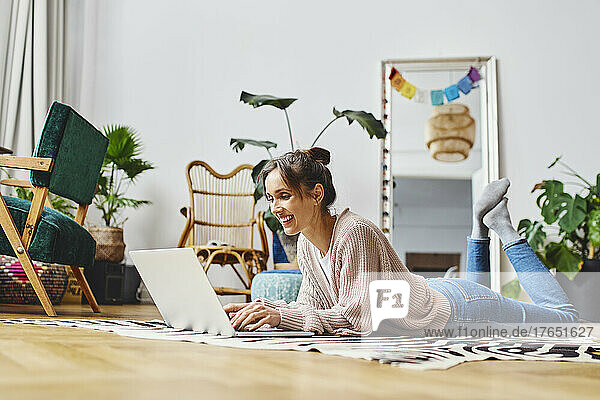 Happy woman using laptop lying down at home