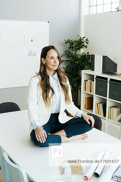 Businesswoman sitting cross-legged on desk in office
