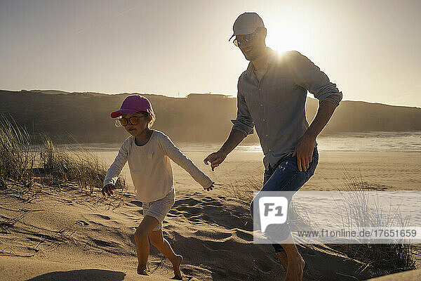 Happy father with daughter running on sand at sunset