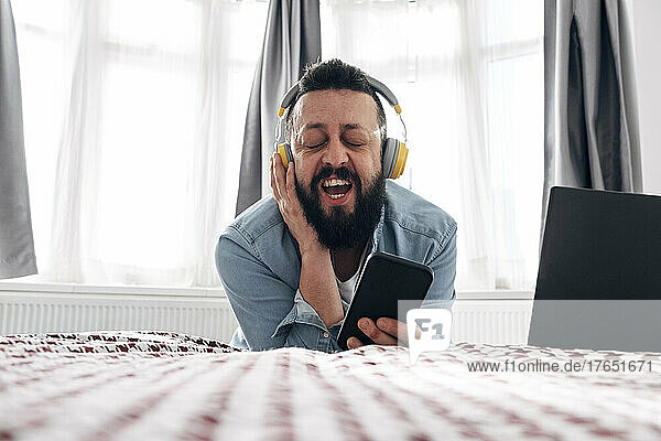 Man listening music through wireless headphones on bed at home