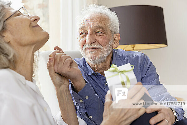 Älterer Mann schaut Frau an  die mit Geschenk in Hotelwohnung sitzt