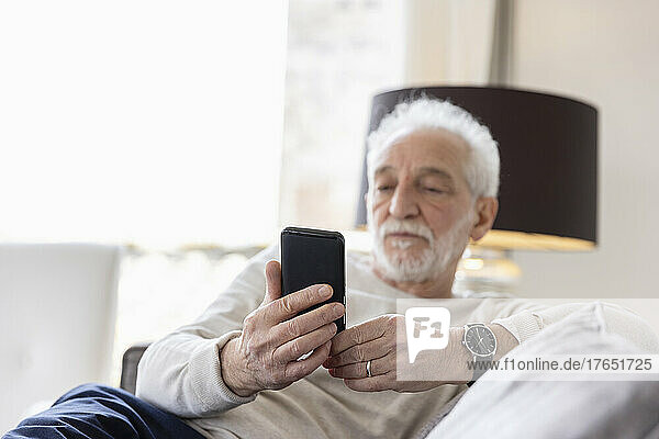 Senior man using smart phone sitting on sofa at hotel apartment
