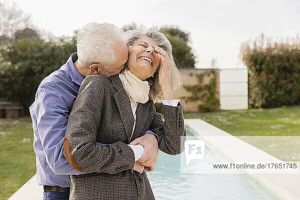 Senior man embracing cheerful woman in front of swimming pool