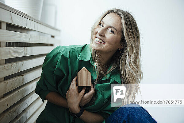 Happy woman holding wooden house model sitting at home
