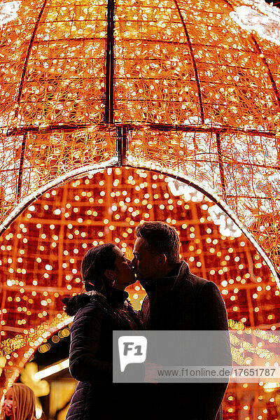 Paar küsst sich vor Weihnachtsbeleuchtung auf den Mund