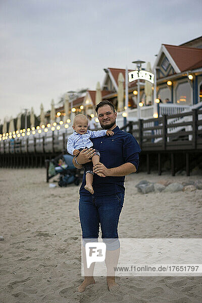 Lächelnder Vater und Sohn stehen im Sand am Strand
