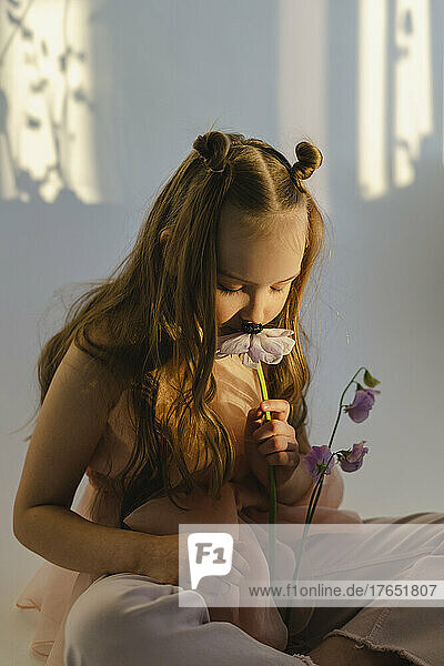 Girl smelling fresh flowers sitting in front of white wall