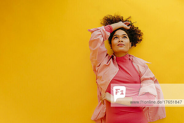 Beautiful woman with hand raised lying on yellow background