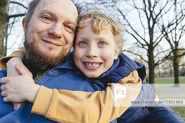 Smiling boy embracing father in public park