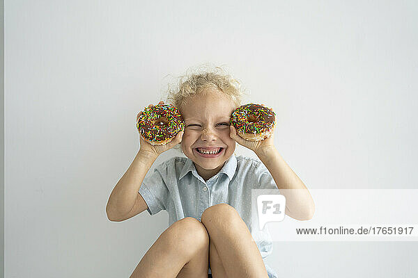 Happy girl holding doughnuts sitting in front of wall