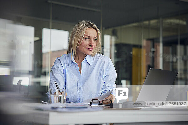 Businesswoman looking at laptop writing in paper at desk in office